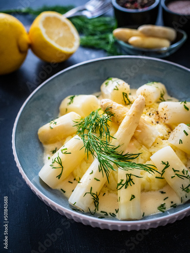 White boiled asparagus in hollandaise sauce with potato puree served on wooden black table 