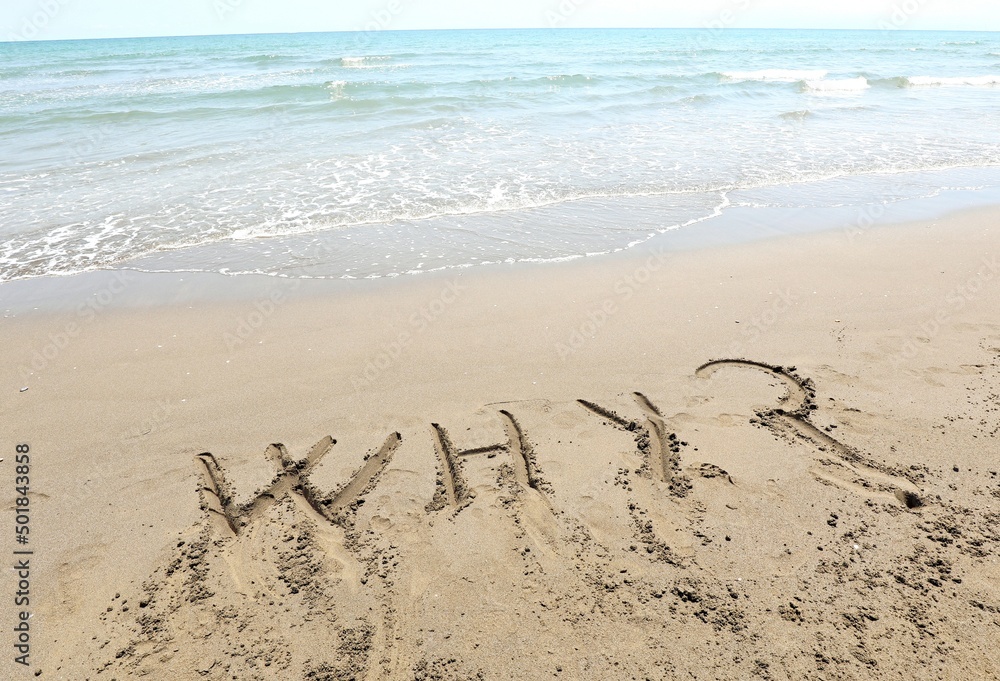 text WHY with question mark that was written in the sand by the sea