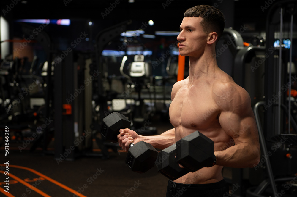 Shirtless man doing bicep curls with dumbbells in gym, biceps workout