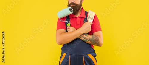 cropped man in work clothes hold paint roller and brush on yellow background photo