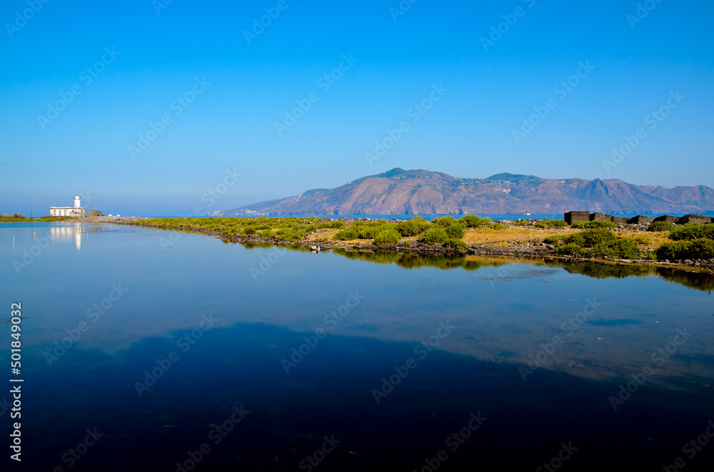 The lighthouse of Punta Lingua across a pond on the island of Salina in the Aeolian Islands, Sicily, Italy