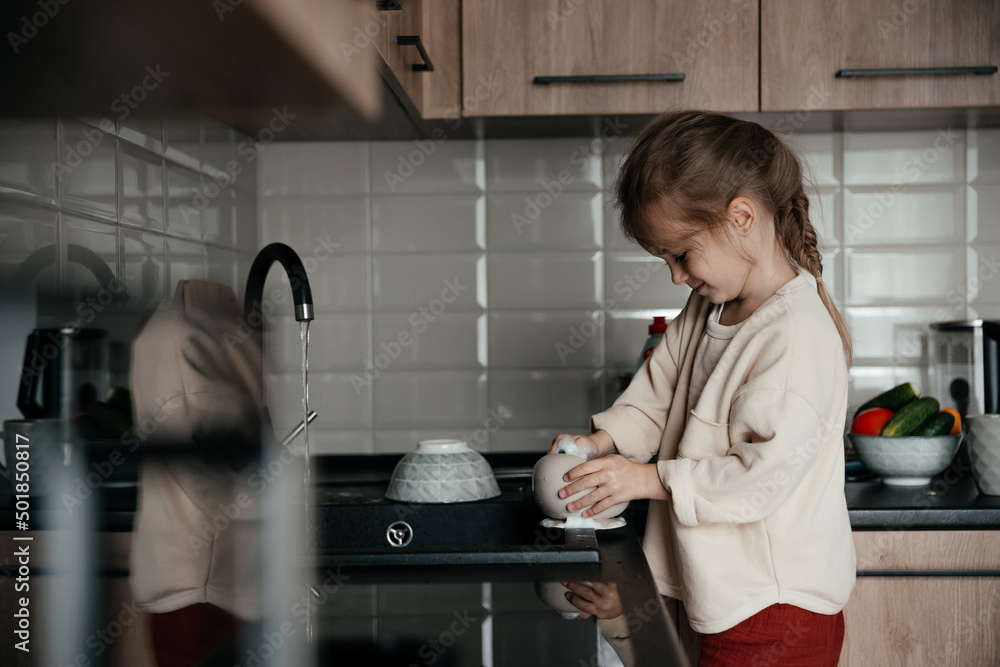 little smiling girl helps with household chores, washes dishes in the kitchen little smiling girl helps with household chores, washes dishes in the kitchen