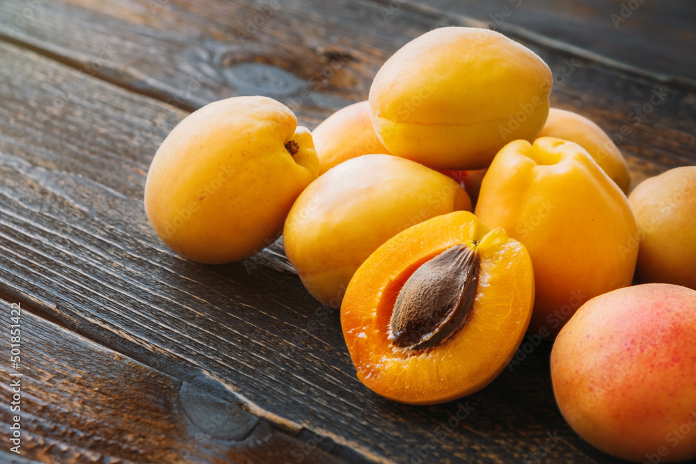 Several apricots from home garden on wooden table. One apricot cut in half.