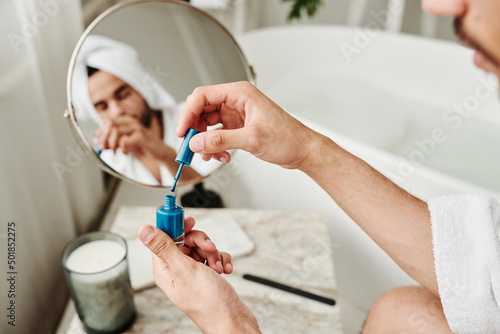Close-up of young man opening blue varnish and painting his nails after bath procedure