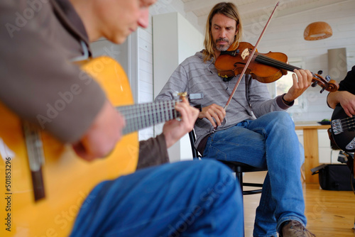 Middle-aged musicians playing guitar, bass and violin during a rehearsal.
