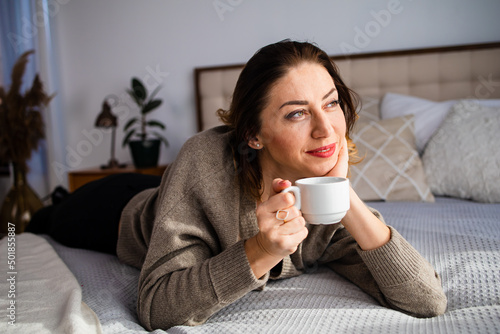 Beautiful middle age woman rest on bed look at the camera. Successful middle aged woman smiling at home.