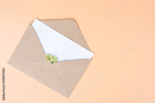 Opened paper envelope with white paper empty note with tiny white blossoming flowers inside, mock up with copy space.Vertical photo.Concept of spring coming, holidays, good news and love emotion