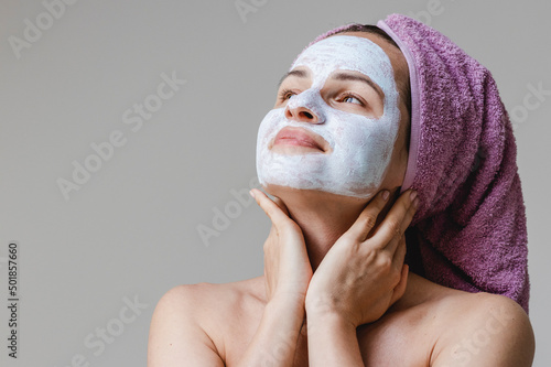Canvas Print Beautiful young woman with facial skin cosmetics cleansing mask on face looking at herself in mirror