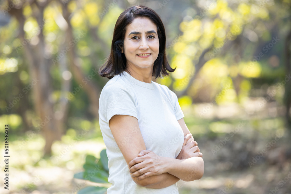 Confident mature urban indian woman wearing white t-shirt standing cross arms in the park outdoors, Smiling asian female with positive expression posing. Copy space. Confident mature urban indian woman wearing white t-shirt standing cross arms in the park outdoors, Smiling asian female with positive expression posing. Copy space.