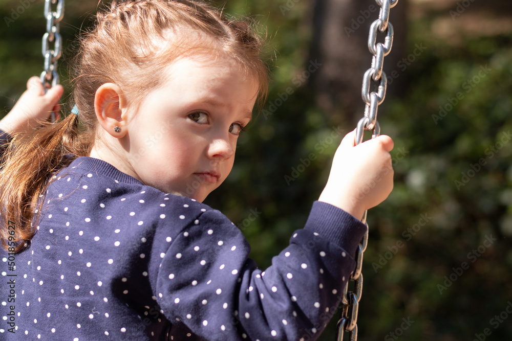 Little cute girl turned around swinging on a swing outdoors on a blurred background Little cute girl turned around swinging on a swing outdoors on a blurred background
