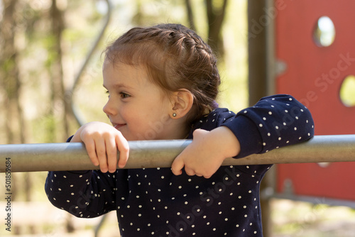 Little beautiful girl smiling look sideways climbing up the pipe on the playground