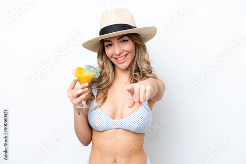 Young woman holding cocktail and wearing a bikini isolated on white background points finger at you with a confident expression
