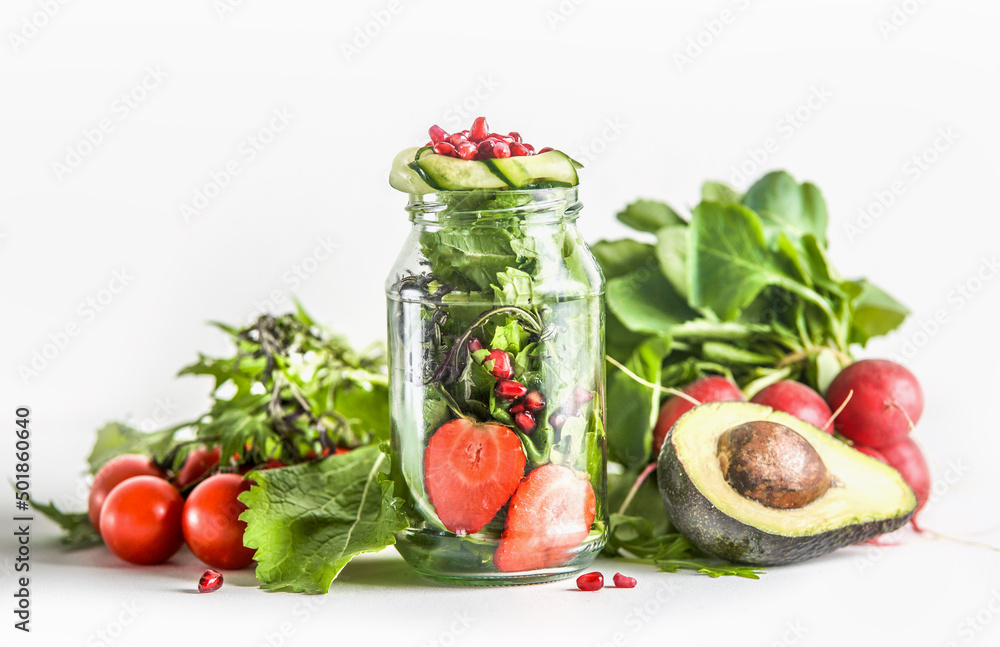 Green salad in jar with ingredients: green lettuce leaves, tomato, strawberry, avocado, cucumber and pomegranate seeds at white background. Healthy to go food with vegetables and fruits. Front view. Green salad in jar with ingredients: green lettuce leaves, tomato, strawberry, avocado, cucumber and pomegranate seeds at white background. Healthy to go food with vegetables and fruits. Front view.