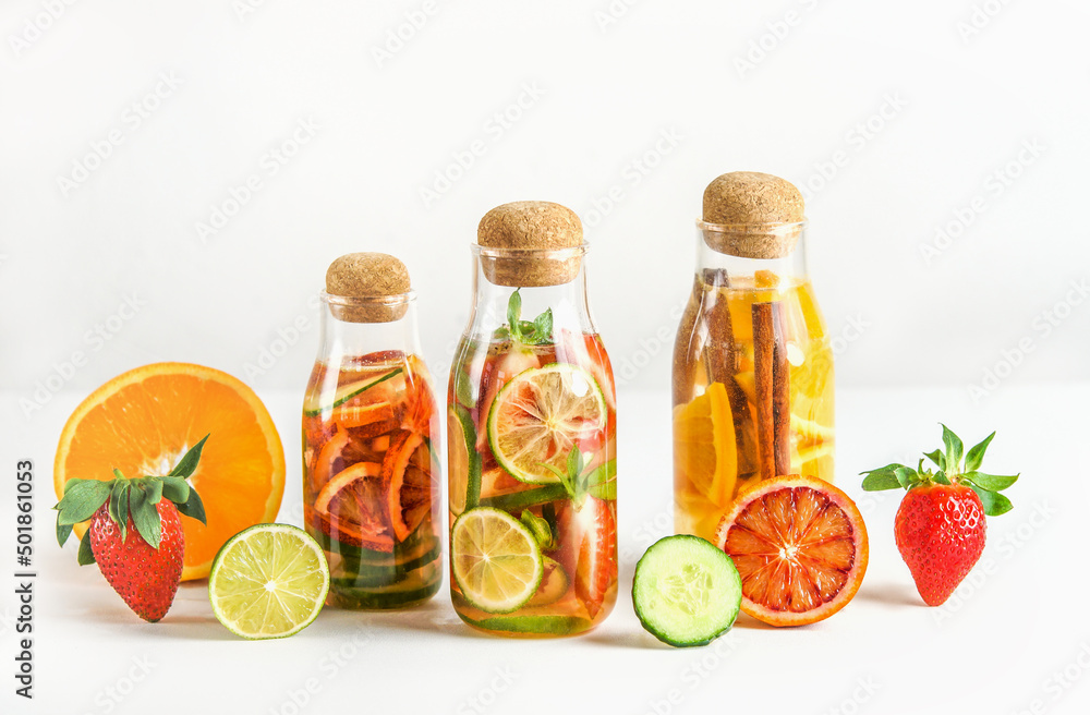 Fruits flavored infused water in glass bottles with ingredients: lime, strawberry, orange, cinnamon and cucumber at white background. Healthy lifestyle with refreshing natural drinks. Front view. Fruits flavored infused water in glass bottles with ingredients: lime, strawberry, orange, cinnamon and cucumber at white background. Healthy lifestyle with refreshing natural drinks. Front view.