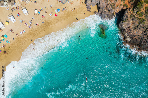 aerial shooting from a drone on a sandy beach with people sunbathing and relaxing. Flat view of the shore and turquoise waves of the surf and people bathing