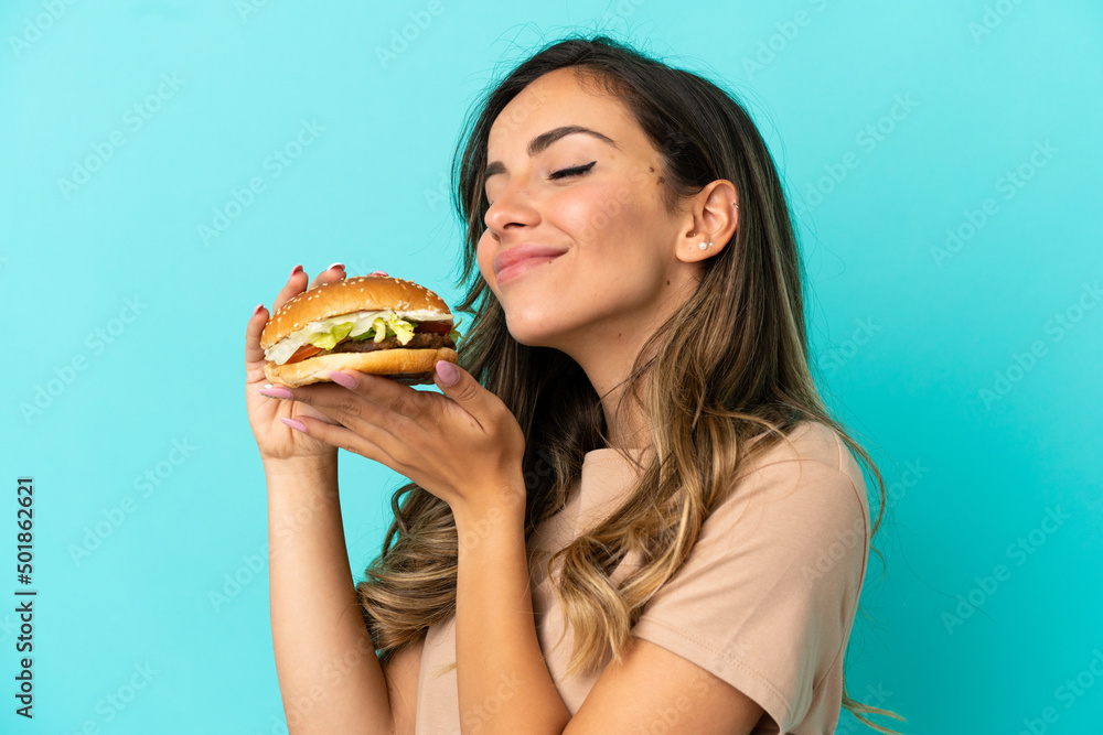 Young woman holding a burger over isolated background Young woman holding a burger over isolated background