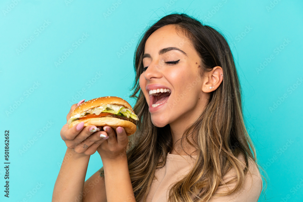 Young woman holding a burger over isolated background Young woman holding a burger over isolated background