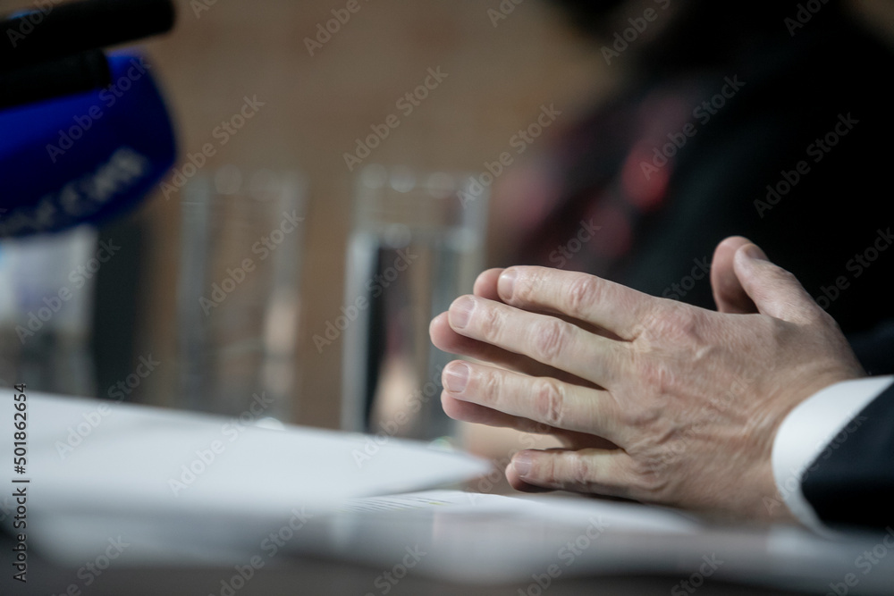 Politician with clasped hands sitting behind desk.