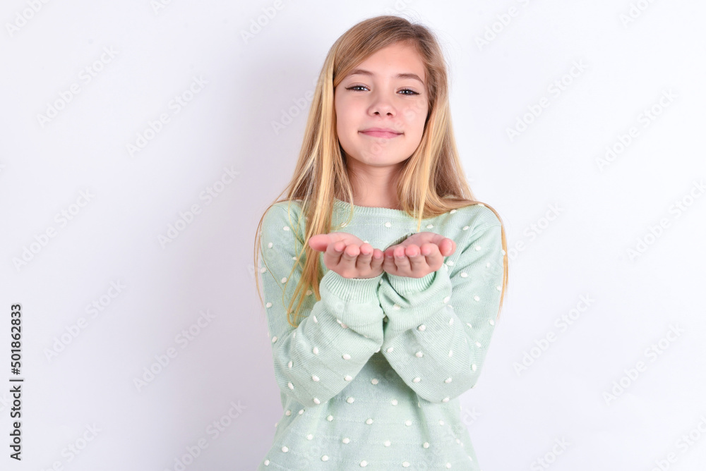 little caucasian kid girl wearing fashion sweater over blue background holding something with open palms, offering to the camera. little caucasian kid girl wearing fashion sweater over blue background holding something with open palms, offering to the camera.