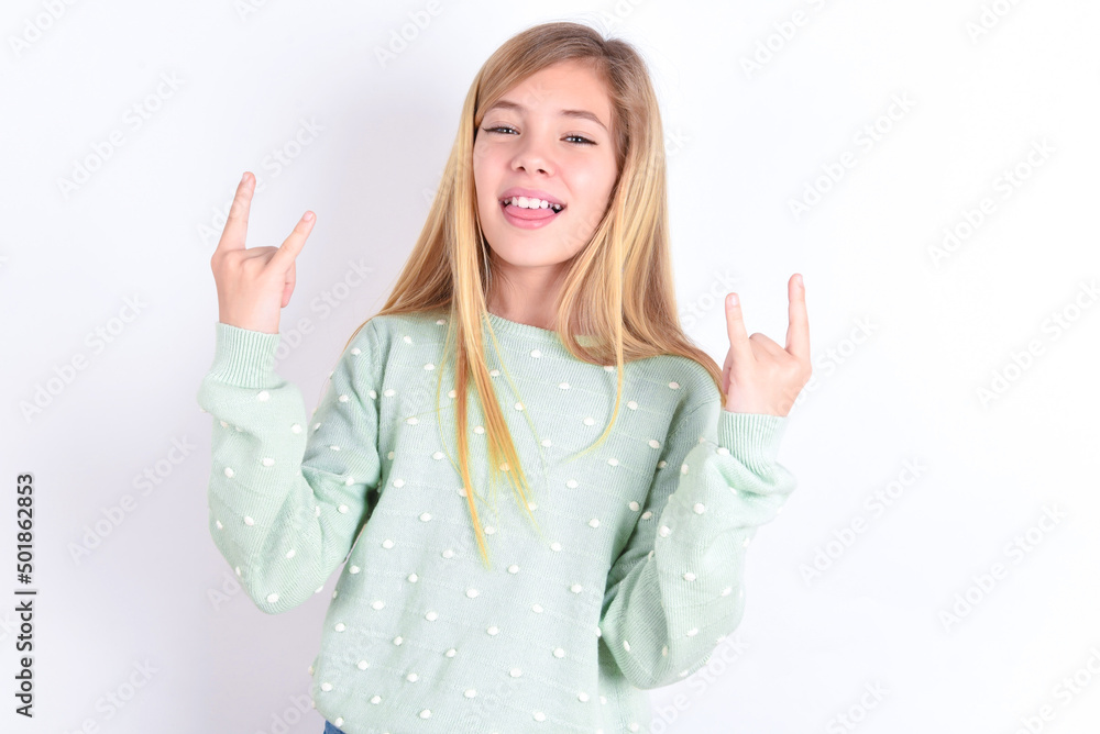 little caucasian kid girl wearing fashion sweater over blue background making rock hand gesture and showing tongue little caucasian kid girl wearing fashion sweater over blue background making rock hand gesture and showing tongue