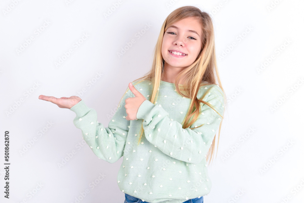 little caucasian kid girl wearing fashion sweater over blue background Showing palm hand and doing ok gesture with thumbs up, smiling happy and cheerful.