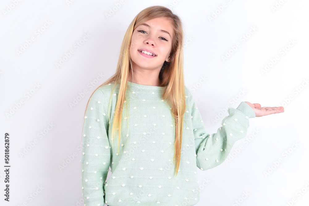 little caucasian kid girl wearing fashion sweater over blue background smiling cheerful presenting and pointing with palm of hand looking at the camera. little caucasian kid girl wearing fashion sweater over blue background smiling cheerful presenting and pointing with palm of hand looking at the camera.