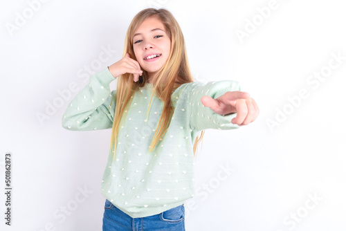 little caucasian kid girl wearing fashion sweater over blue background smiling cheerfully and pointing to camera while making a call you later gesture, talking on phone