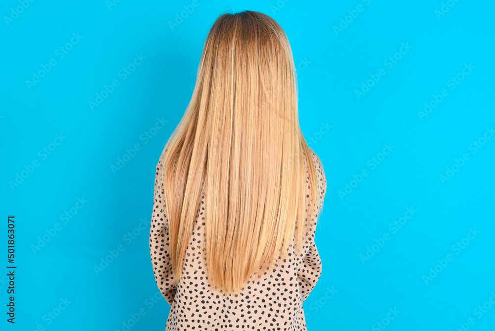 The back view of a little caucasian kid girl wearing animal print sweater over blue background . Studio Shoot. The back view of a little caucasian kid girl wearing animal print sweater over blue background . Studio Shoot.