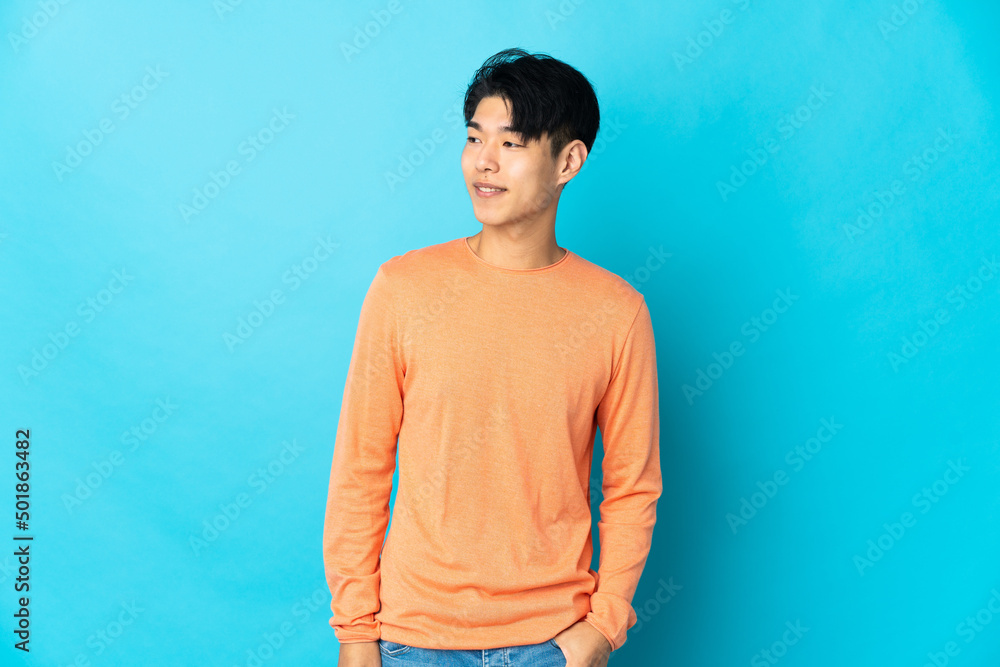 Young Chinese man isolated on blue background looking to the side and smiling Young Chinese man isolated on blue background looking to the side and smiling