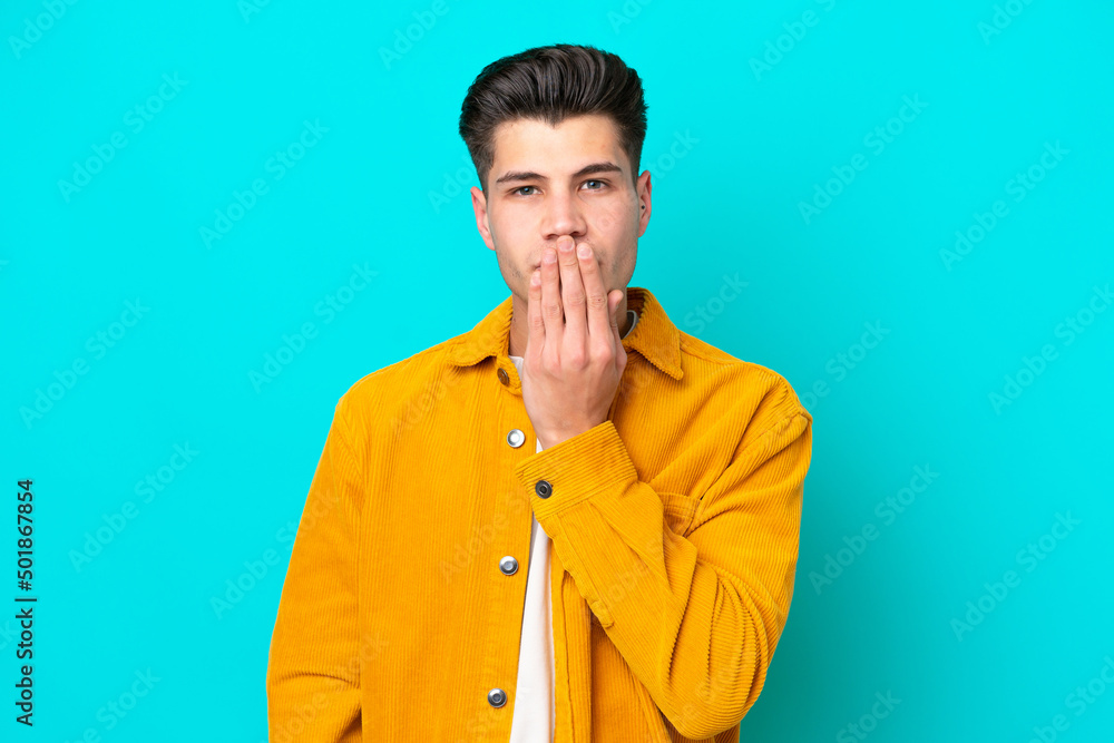 Young handsome caucasian man isolated on blue bakcground covering mouth with hand Young handsome caucasian man isolated on blue bakcground covering mouth with hand