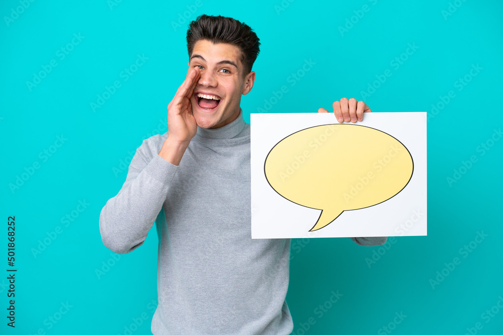 Young handsome caucasian man isolated on blue bakcground holding a placard with speech bubble icon and shouting Young handsome caucasian man isolated on blue bakcground holding a placard with speech bubble icon and shouting