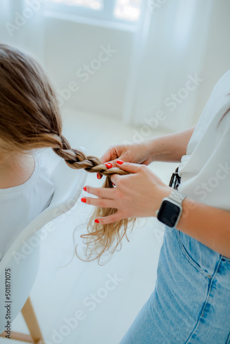 Mom and daughter spend time together. Happiness and joy. A mother weaving braids out of hair of little girl's hair.