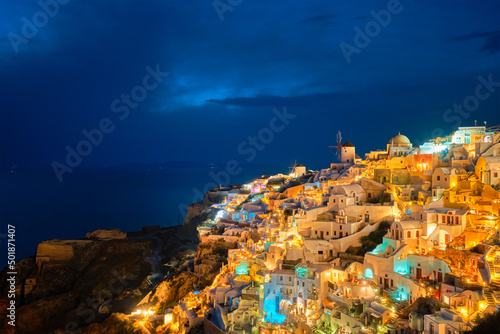 Famous greek iconic picturesque tourist destination Oia village with traditional white houses and windmills in Santorini island in the evening blue hour, Greece