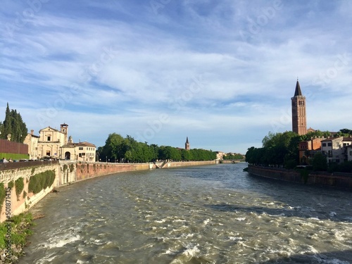 Adige river view from Ponte Pietra. Tower bell of Saint Anastasia church and facades of medieval buildings. Selective focus. Verona, Italy