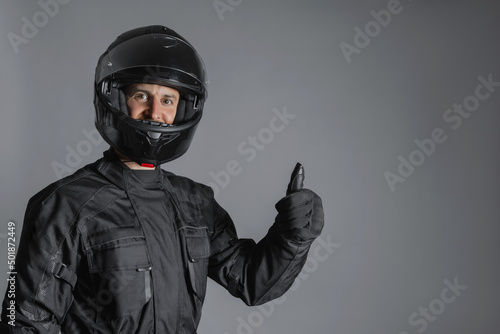 Man wearing protective black motorcycling equipment, with thumb up, indoors. © BASILICOSTUDIO STOCK