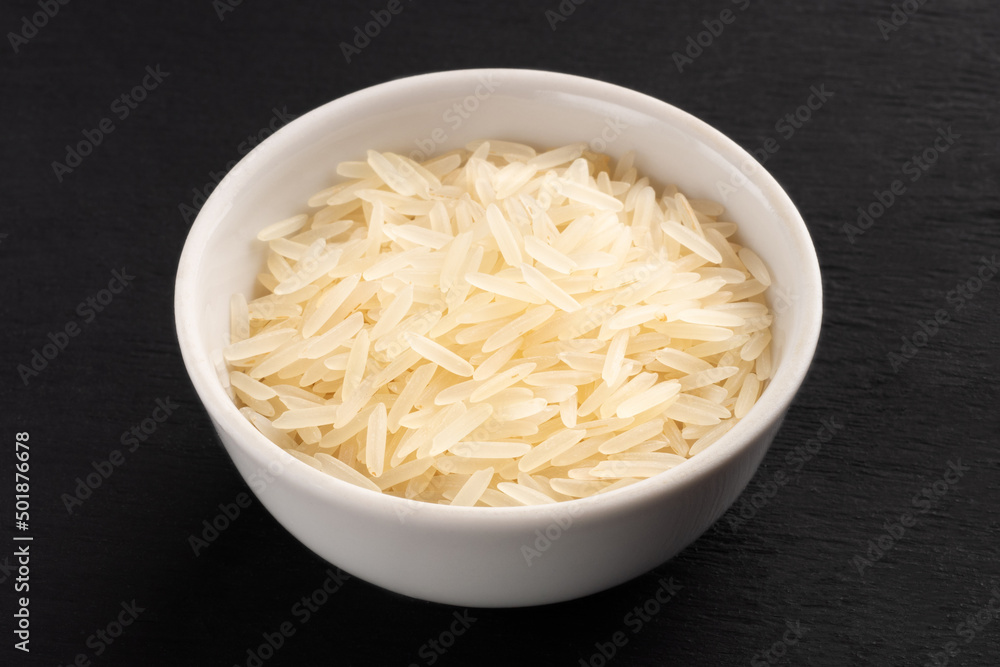 Long Basmati rice in ceramic bowl on black wooden background. Macro. Vegetarian food concept
