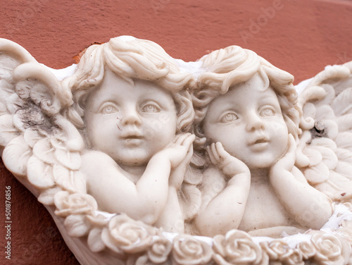 Two baby angels with wings marble sculpture on red wall of building. Close-up, front view. © Анастасия Бурлакова