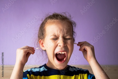girl child in a striped turtleneck shows pain due to a cotton stick in the ear, where it is very dirty