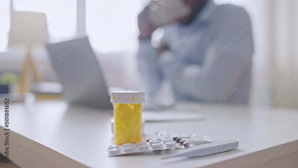 Pills lying on desk, ill office worker typing on laptop, working despite illness Pills lying on desk, ill office worker typing on laptop, working despite illness