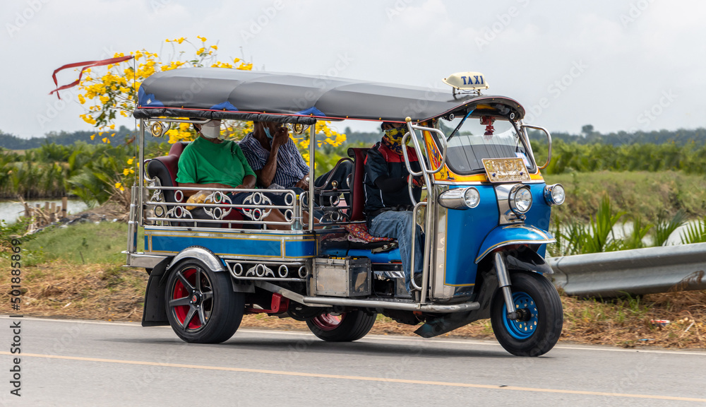 Obraz premium A traditional motor tricycle - tuk tuk rides on a rural road,Thailand