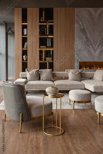 living room, marble wall fireplace and stylish bookcase in chic expensive interior of luxury country house with a modern design with wood and led light, gray furniture with gold elements