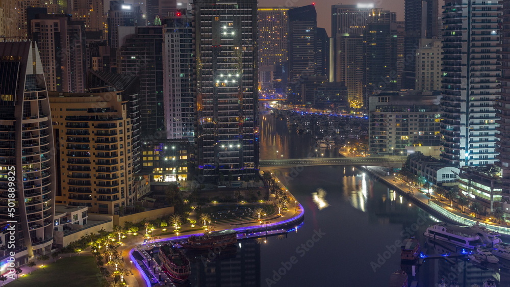 Obraz premium Dubai Marina with several boats and yachts parked in harbor and skyscrapers around canal aerial night to day timelapse.