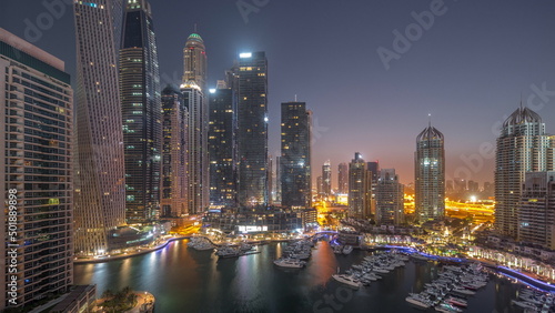 Dubai marina tallest skyscrapers and yachts in harbor aerial night to day timelapse.