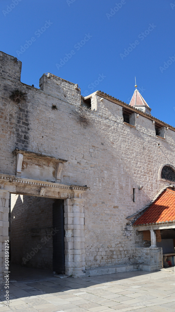 The southern city gate of Trogir and the remains of the city wall on a sunny summer day. Medieval architecture in the historical part of the old town of Trogir, Dalmatia, Croatia