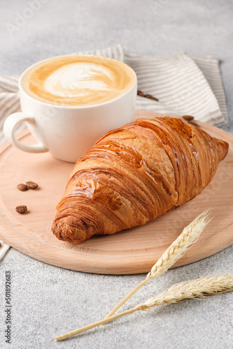 Large croissant and a cup of cappuccino on a light background