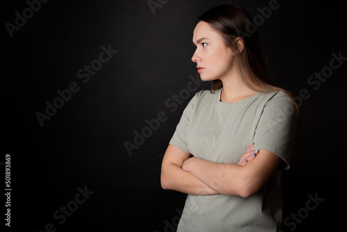Suspicions, a look from the left. A young brunette woman in a T-shirt, experiencing distrust and doubt, portrait on black