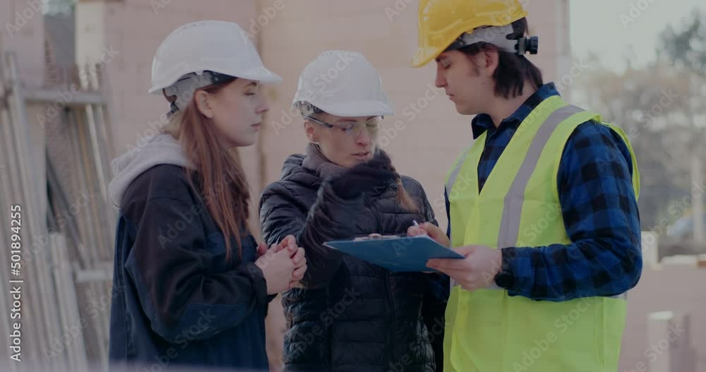 Female architect and engineer discussing over clipboard with male coworker Female architect and engineer discussing over clipboard with male coworker