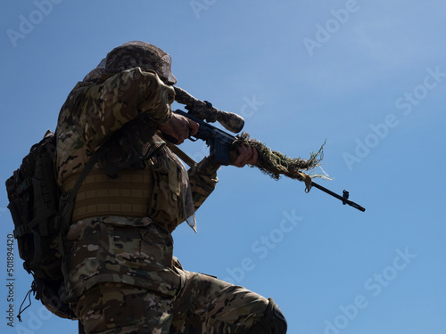 A professional special forces sniper during a special operation - aims at the enemy against the blue sky.