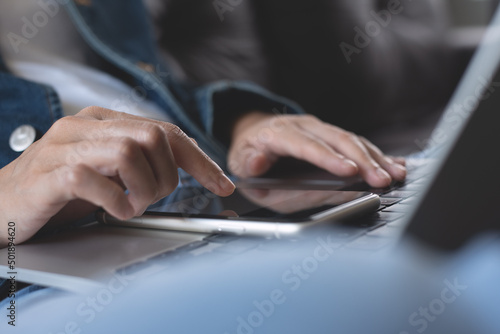 Young casual woman sitting on sofa using mobile phone and laptop computer at home, close up