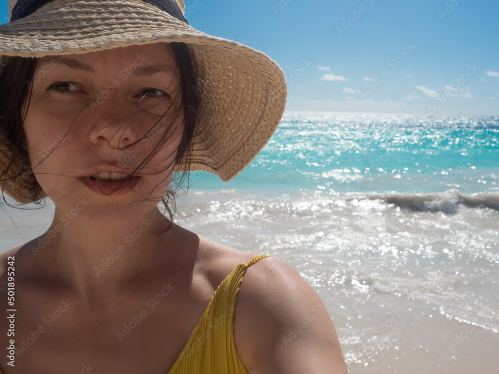 A happy traveler in a straw hat on a beach with white sand and clear azure water. Vacation on a tropical island by the sea